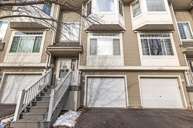 townhome / multi-family property with an attached garage, a shingled roof, and driveway