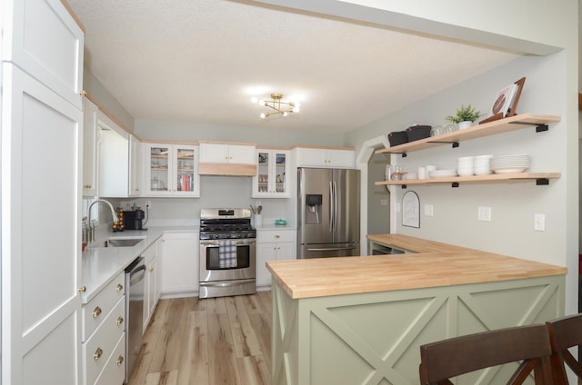 kitchen with a sink, stainless steel appliances, a peninsula, light wood-type flooring, and butcher block counters