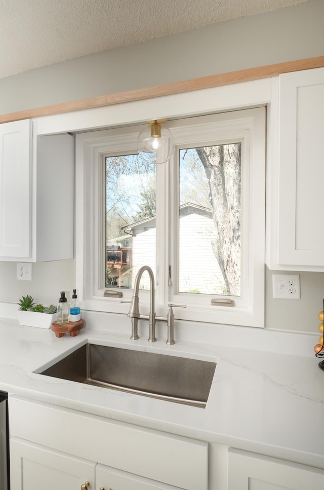 kitchen featuring a sink, white cabinets, light stone countertops, and a textured ceiling