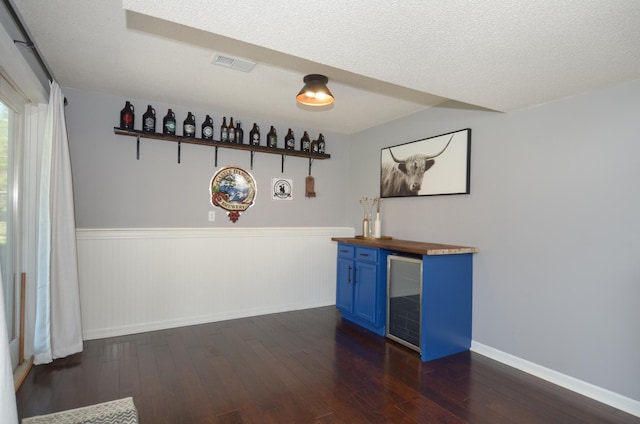 unfurnished dining area with a bar, wainscoting, dark wood finished floors, and visible vents