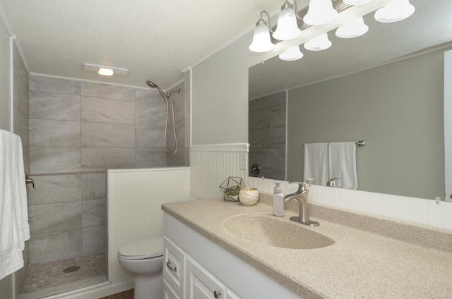 bathroom with wainscoting, a tile shower, vanity, toilet, and a textured ceiling