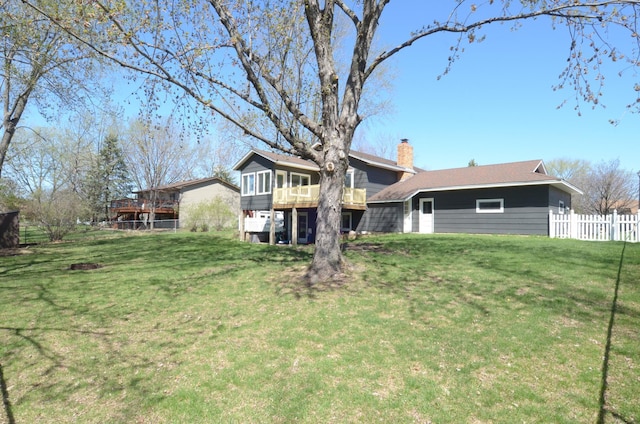rear view of house with a lawn, a wooden deck, fence, and a chimney