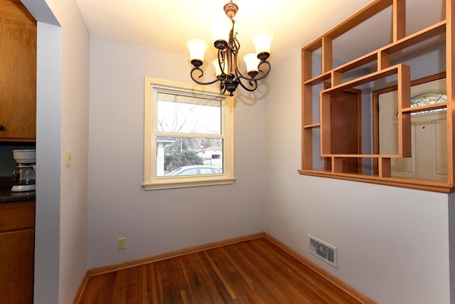 empty room with dark hardwood / wood-style floors and a chandelier