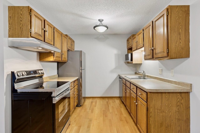 kitchen featuring appliances with stainless steel finishes, sink, a textured ceiling, and light wood-type flooring