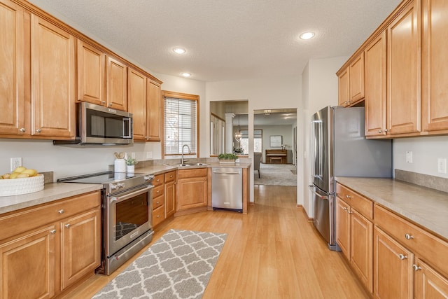 kitchen with appliances with stainless steel finishes, sink, light hardwood / wood-style flooring, and a textured ceiling