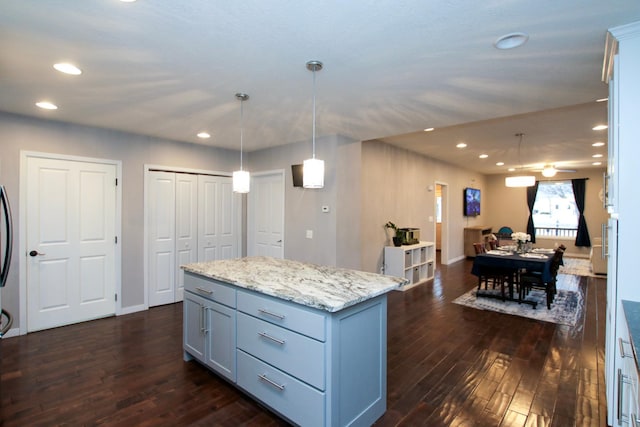 kitchen with decorative light fixtures, dark wood-type flooring, light stone countertops, and a kitchen island