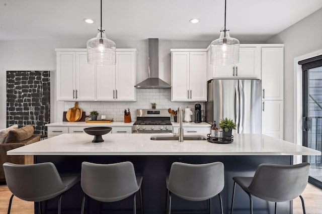 kitchen with white cabinets, an island with sink, wall chimney exhaust hood, and appliances with stainless steel finishes