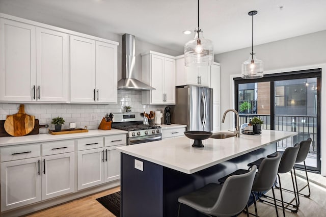 kitchen with white cabinetry, appliances with stainless steel finishes, wall chimney range hood, and an island with sink