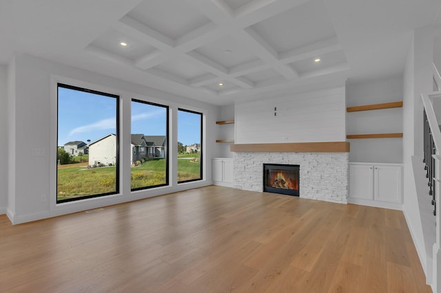 unfurnished living room featuring coffered ceiling, light wood-type flooring, beam ceiling, and a stone fireplace