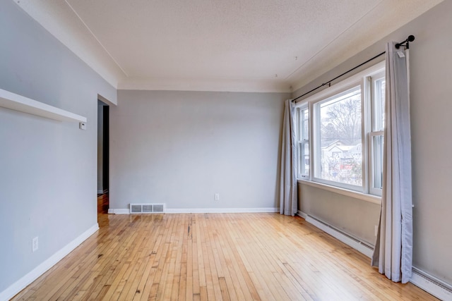 empty room featuring light hardwood / wood-style flooring, a baseboard heating unit, and a textured ceiling