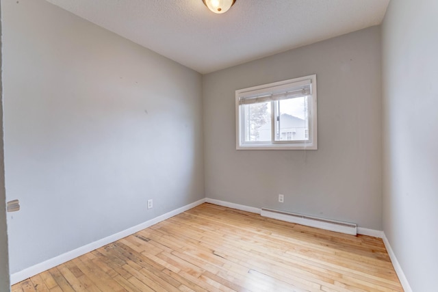 spare room featuring baseboard heating, light hardwood / wood-style floors, and a textured ceiling