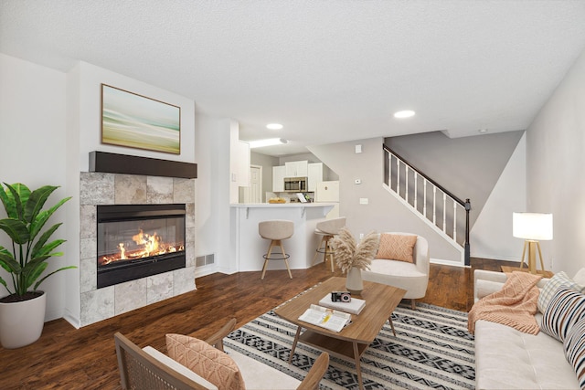 living room with a tiled fireplace, dark wood-type flooring, and a textured ceiling