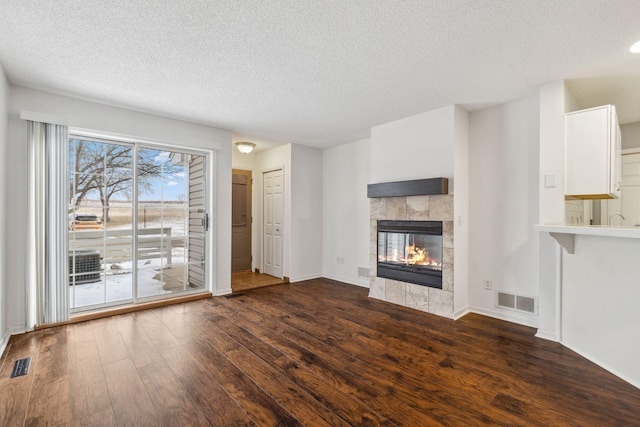 unfurnished living room with dark wood-type flooring, a tile fireplace, and a textured ceiling