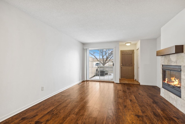 unfurnished living room featuring a tiled fireplace, a textured ceiling, and dark hardwood / wood-style flooring