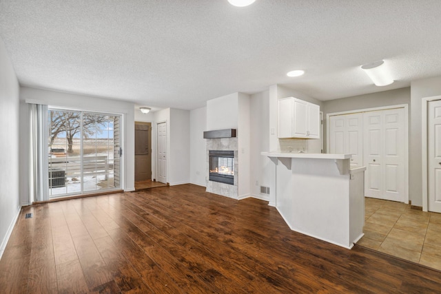 kitchen with white cabinetry, dark hardwood / wood-style floors, a kitchen bar, a tiled fireplace, and kitchen peninsula