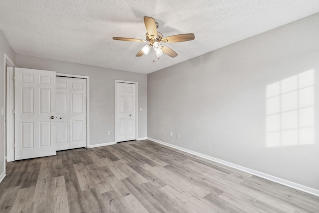 unfurnished bedroom with ceiling fan, two closets, a textured ceiling, and light hardwood / wood-style floors