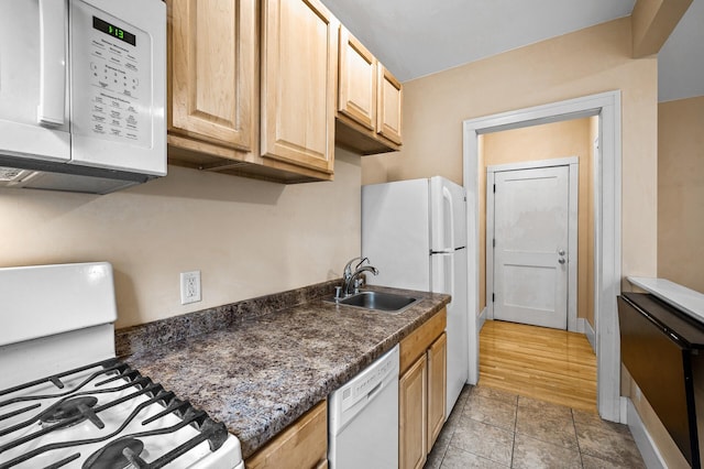 kitchen with sink, light brown cabinetry, white appliances, and dark stone counters