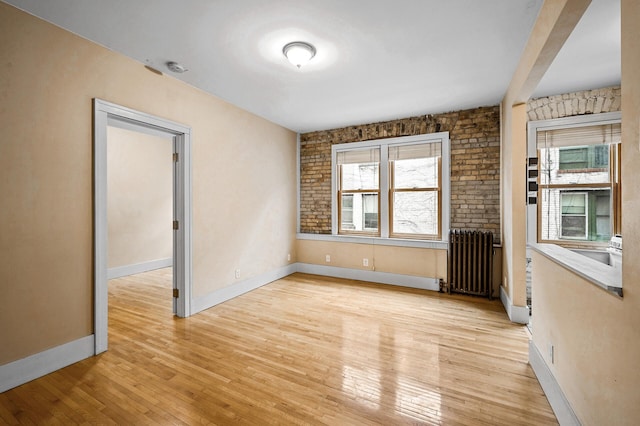 empty room featuring radiator, brick wall, and light wood-type flooring