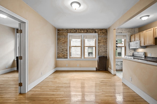 kitchen with light brown cabinetry, range, radiator, brick wall, and light hardwood / wood-style floors