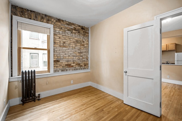 empty room featuring a healthy amount of sunlight, radiator heating unit, and light hardwood / wood-style flooring