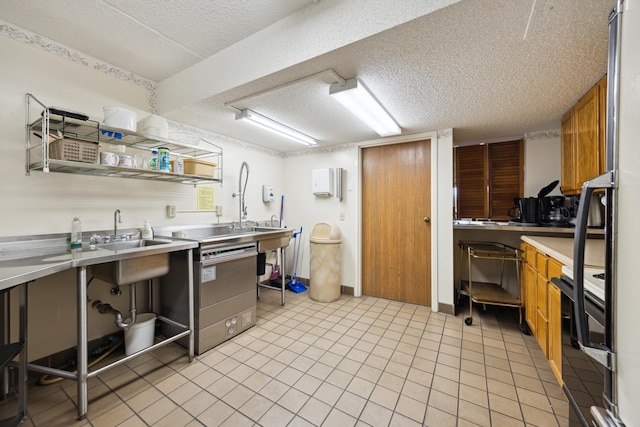 kitchen featuring sink, light tile patterned floors, stove, a textured ceiling, and stainless steel range with electric cooktop