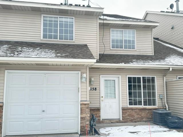 snow covered property entrance with central AC unit and a garage