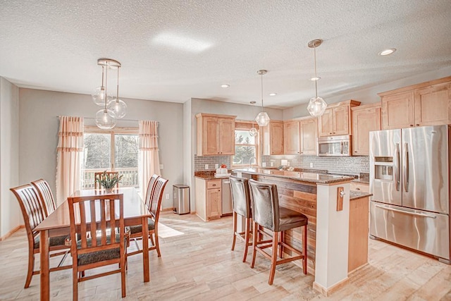 kitchen featuring stone counters, pendant lighting, a center island, stainless steel appliances, and light brown cabinets