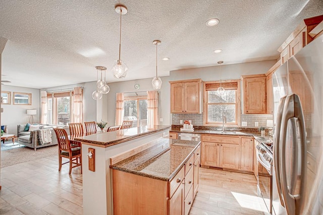 kitchen with pendant lighting, appliances with stainless steel finishes, light brown cabinetry, and a center island