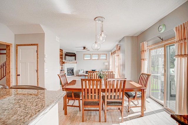 dining space featuring a stone fireplace, light hardwood / wood-style flooring, and a textured ceiling