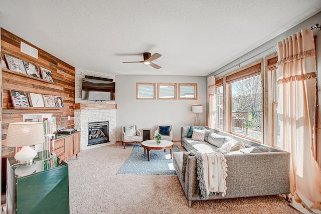 carpeted living room featuring ceiling fan, a fireplace, a textured ceiling, and wood walls