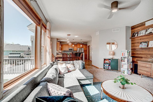 carpeted living room with ceiling fan, a textured ceiling, and wood walls