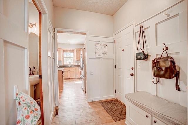 mudroom with sink, a textured ceiling, and light wood-type flooring