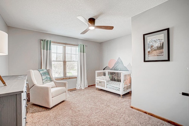 bedroom featuring ceiling fan, light colored carpet, a nursery area, and a textured ceiling