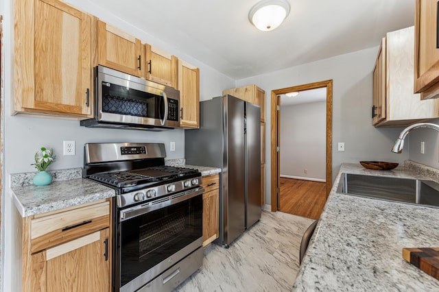 kitchen with stainless steel appliances, light stone countertops, sink, and light brown cabinets