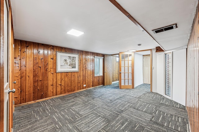 basement with wood walls, french doors, and dark colored carpet