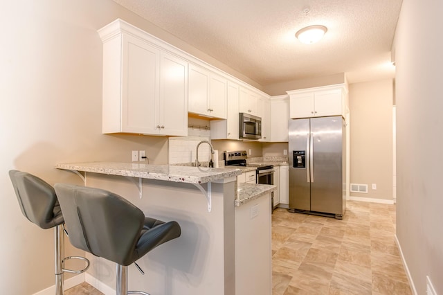 kitchen featuring a kitchen bar, white cabinetry, appliances with stainless steel finishes, kitchen peninsula, and decorative backsplash