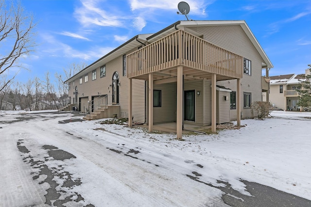 snow covered rear of property with a wooden deck and a garage