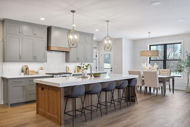 kitchen with a large island, a breakfast bar area, premium range hood, gray cabinetry, and light hardwood / wood-style floors