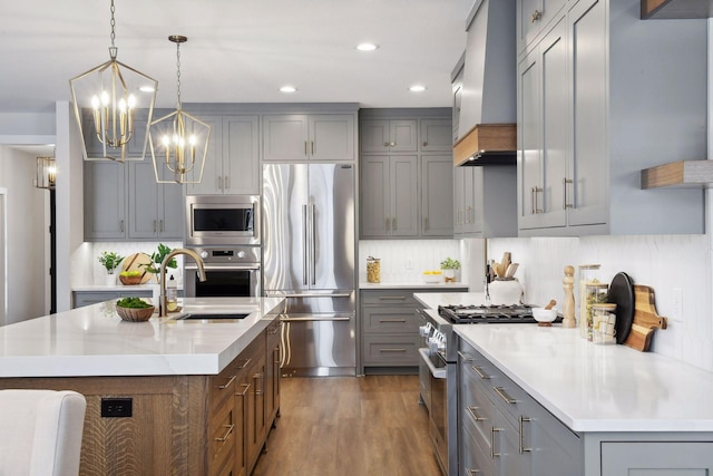 kitchen featuring premium range hood, pendant lighting, sink, a kitchen island with sink, and stainless steel appliances