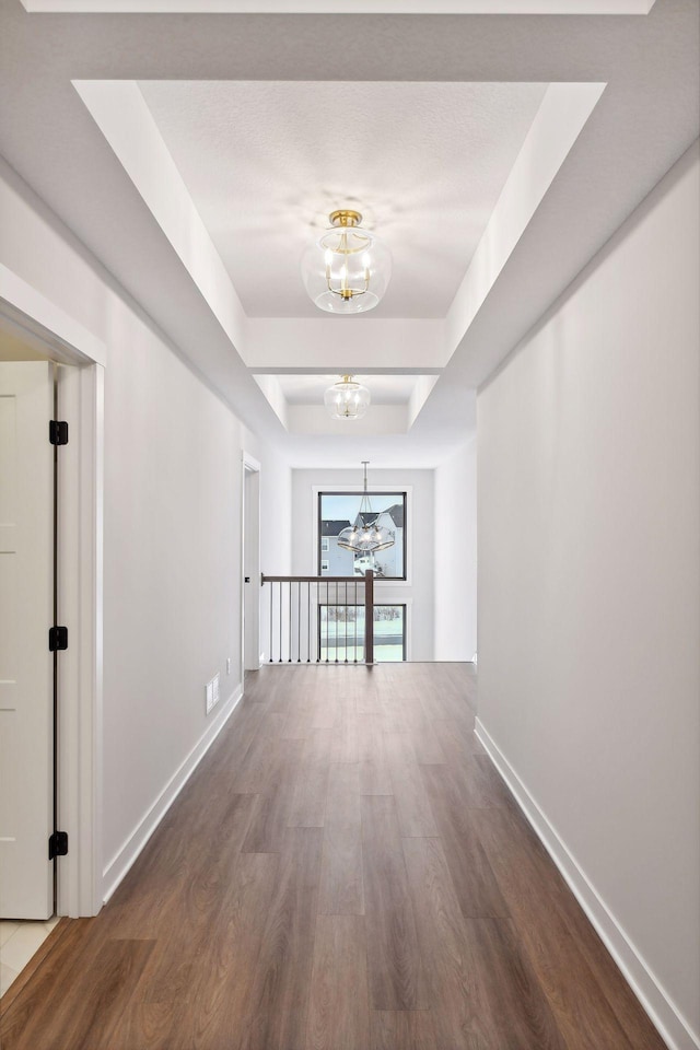 corridor with hardwood / wood-style flooring, a chandelier, and a tray ceiling