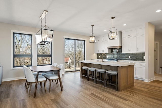 18436 56th Ct N, Plymouth, MN 55446 - kitchen with light countertops, wood finished floors, a kitchen island with sink, white cabinets, and baseboards