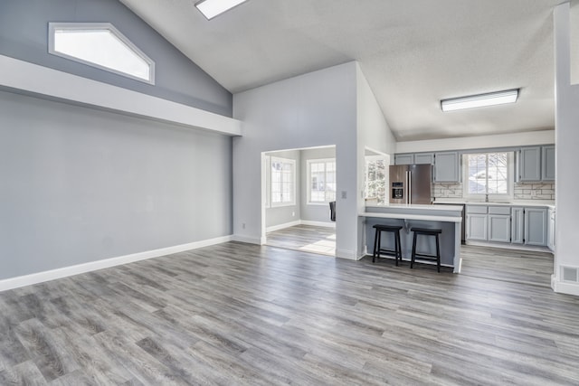 unfurnished living room featuring light wood-type flooring, baseboards, high vaulted ceiling, and a sink