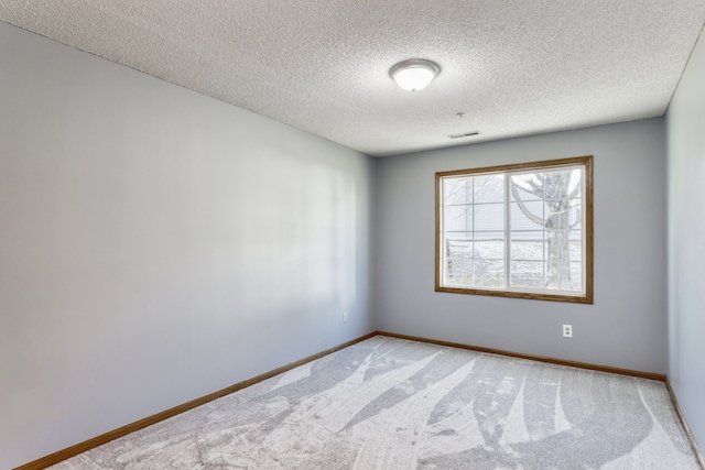 spare room featuring light carpet, a textured ceiling, and baseboards