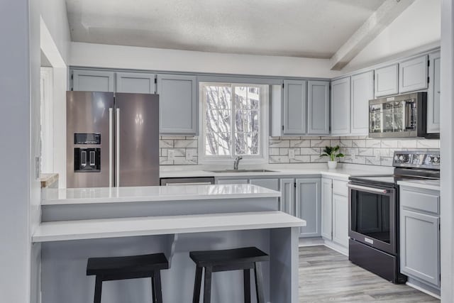 kitchen featuring light countertops, appliances with stainless steel finishes, a kitchen bar, and a sink