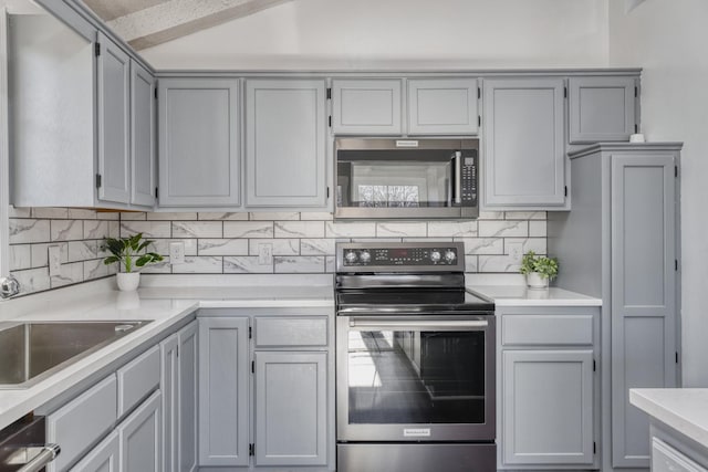 kitchen with tasteful backsplash, appliances with stainless steel finishes, gray cabinets, and sink