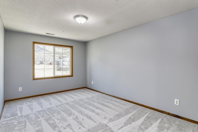 spare room featuring a textured ceiling, light colored carpet, visible vents, and baseboards