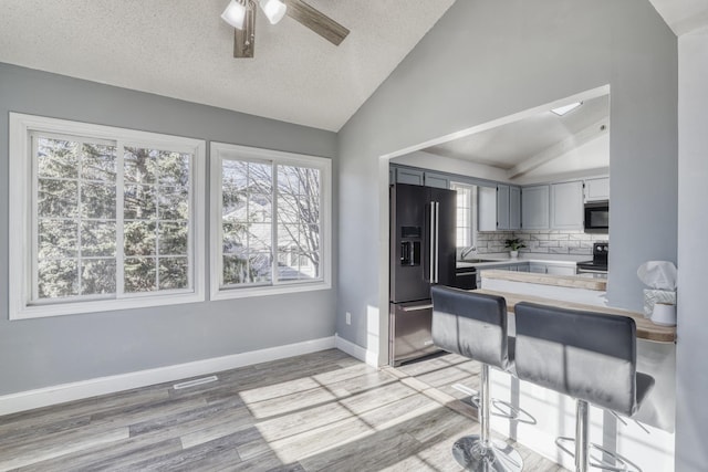 kitchen featuring light countertops, electric range, light wood-style floors, vaulted ceiling, and high end black fridge