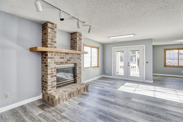 unfurnished living room featuring a brick fireplace, plenty of natural light, french doors, and wood finished floors