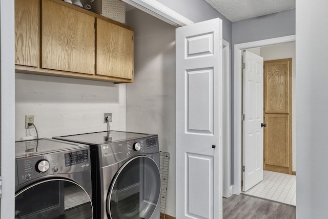 laundry area featuring washer and dryer, cabinet space, a textured ceiling, and wood finished floors