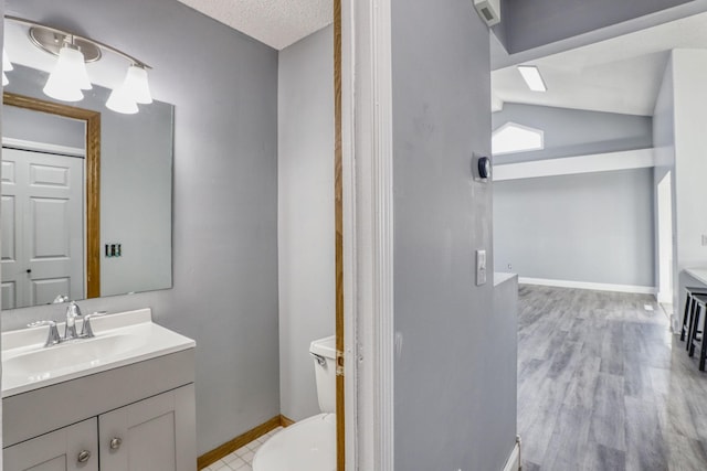 bathroom featuring baseboards, toilet, wood finished floors, vaulted ceiling, and vanity